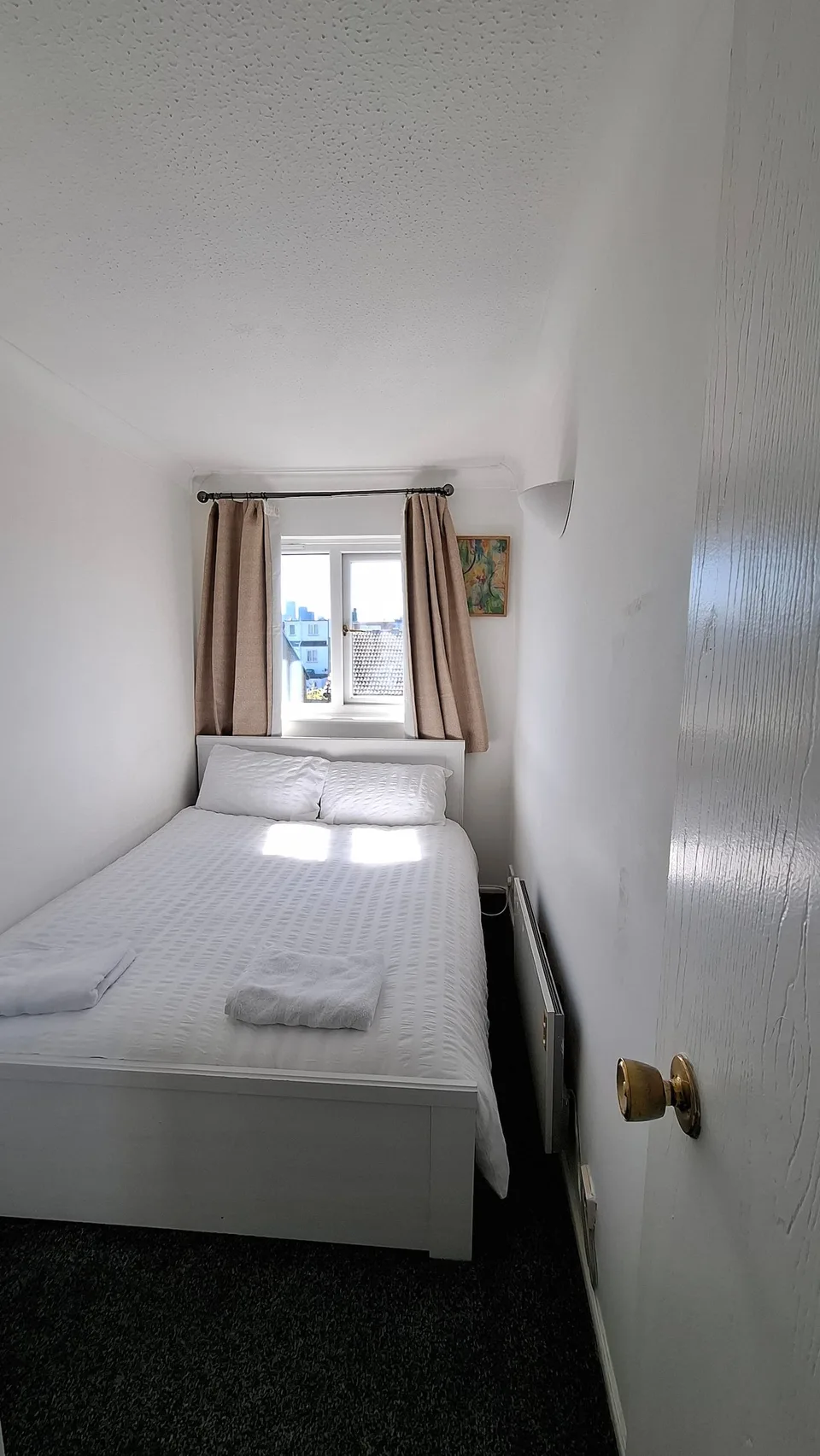 View through a bedroom doorway towards a bed and window